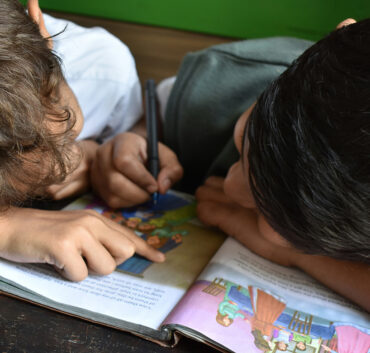 Two children reading and drawing in illustrated book