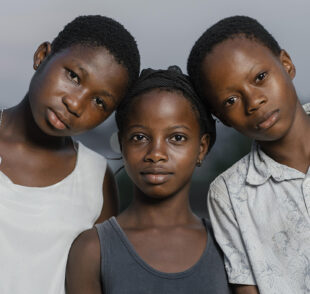 Three children standing shoulder-to-shoulder outdoors.