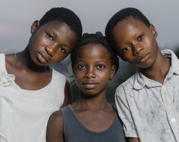 Three children standing shoulder-to-shoulder outdoors.