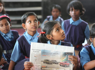 Schoolchildren in classroom reading a newspaper