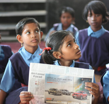 Schoolchildren in classroom reading a newspaper