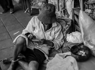 Person sitting on sidewalk surrounded by belongings