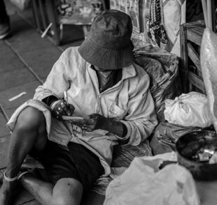 Person sitting on sidewalk surrounded by belongings