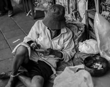 Person sitting on sidewalk surrounded by belongings