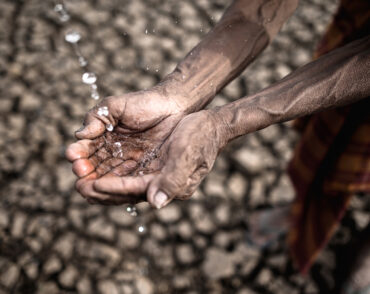 Cupped hands catching water over cracked earth
