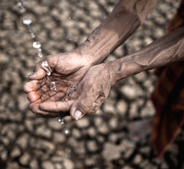 Cupped hands catching water over cracked earth