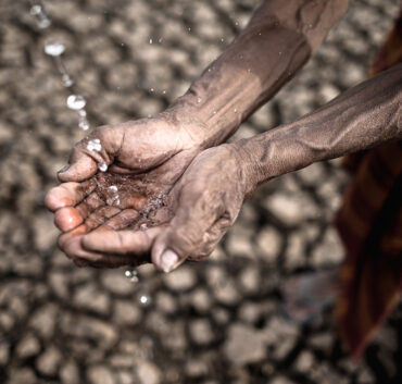 Cupped hands catching water over cracked earth