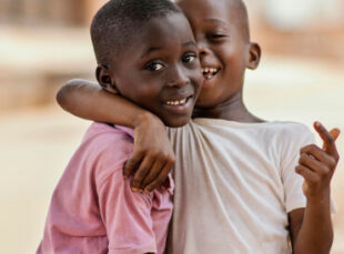 Two smiling children hugging outdoors