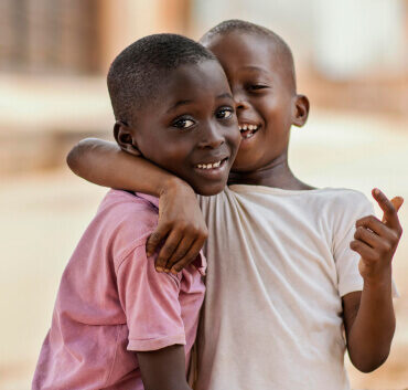 Two smiling children hugging outdoors